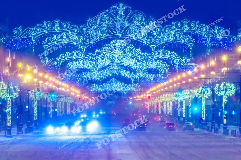 Фотография запечатлела Невский проспект, украшенный новогодними огнями. Световые арки и гирлянды, изящно обрамляющие улицу, подчеркивают архитектурную красоту и создают атмосферу праздника. Вечерний снег добавляет мягкости кадру, а свет фар автомобилей усиливает впечатление оживленного городского ритма.